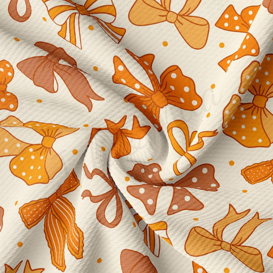 The image is a close-up view of a fabric with a repeating pattern of orange and white bows and polka dots.