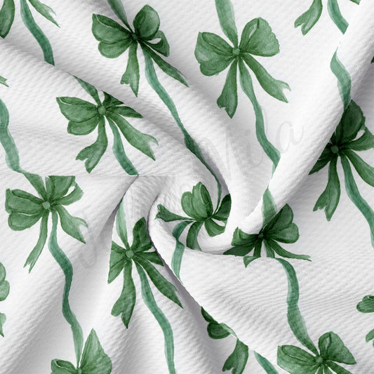 a close-up view of a fabric with a repeating pattern of green bows on a white background.