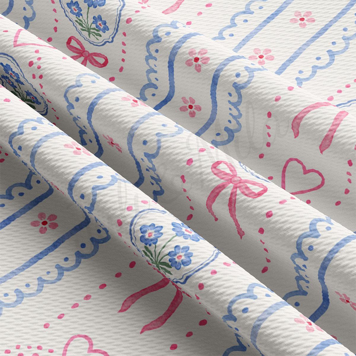 a close-up view of a fabric with a repeating pattern of blue and pink flowers and hearts. The fabric appears to be folded or crumpled, revealing the intricate design underneath.