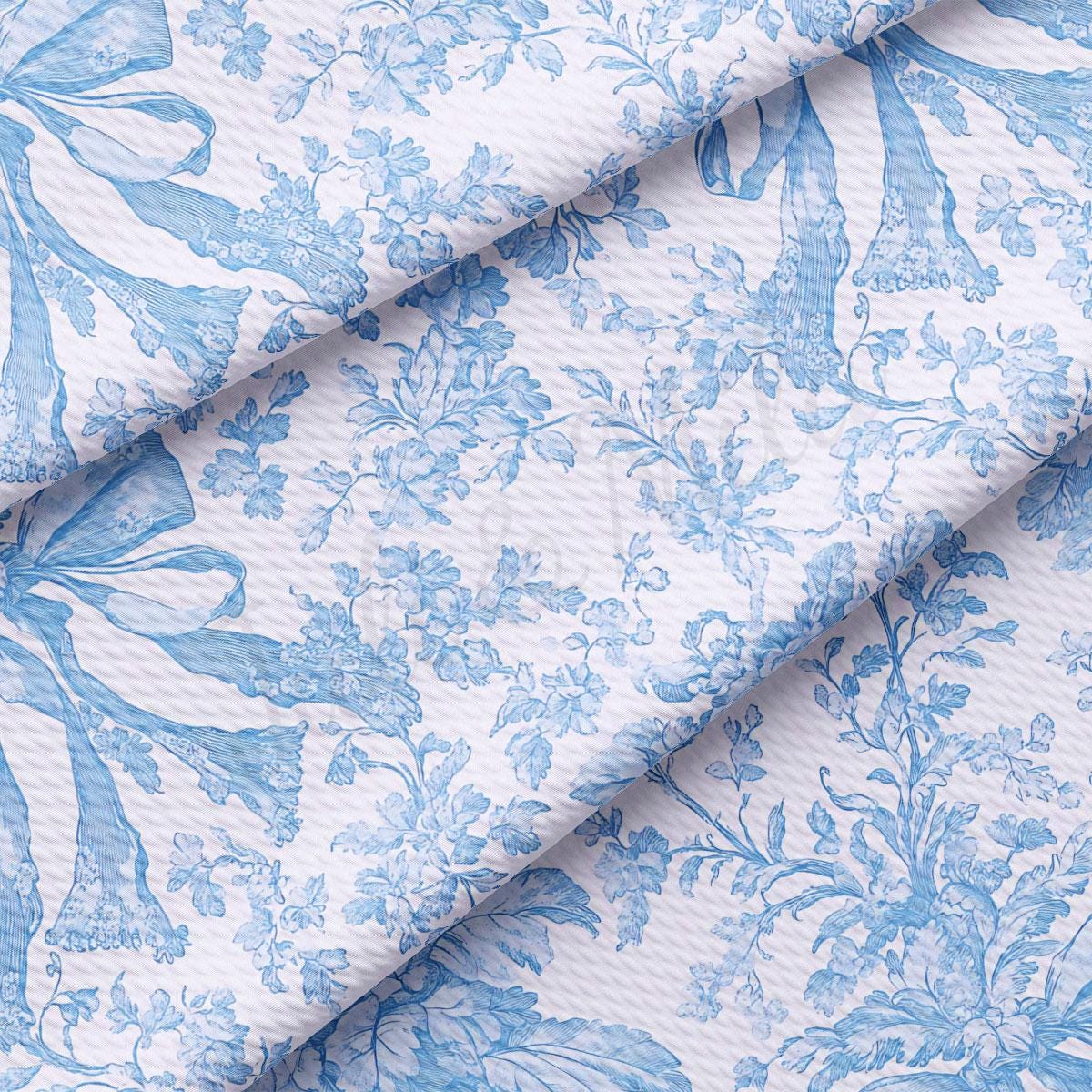 a close-up view of a fabric with a blue floral pattern. The fabric appears to be folded or rolled, revealing the intricate design of the blue flowers and leaves. The pattern is repeated across the fabric, creating a visually appealing and harmonious design.