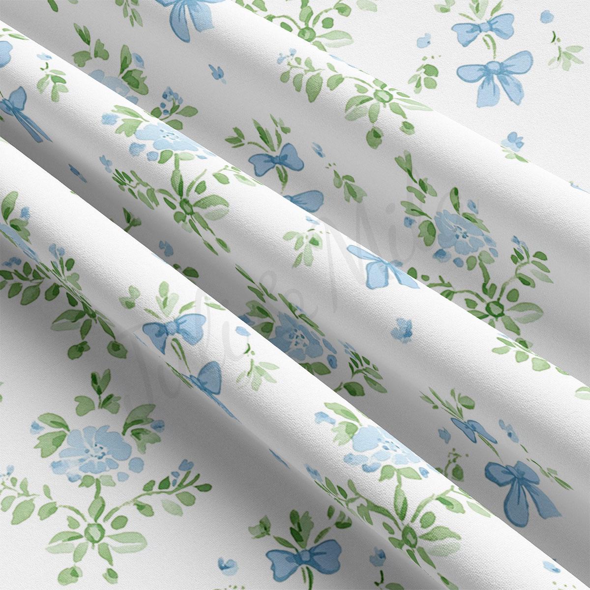 a close-up view of a fabric with a floral pattern in shades of blue and green. The fabric appears to be white, and the pattern consists of various blue flowers and green leaves. The fabric is folded and crumpled, giving it a textured appearance.