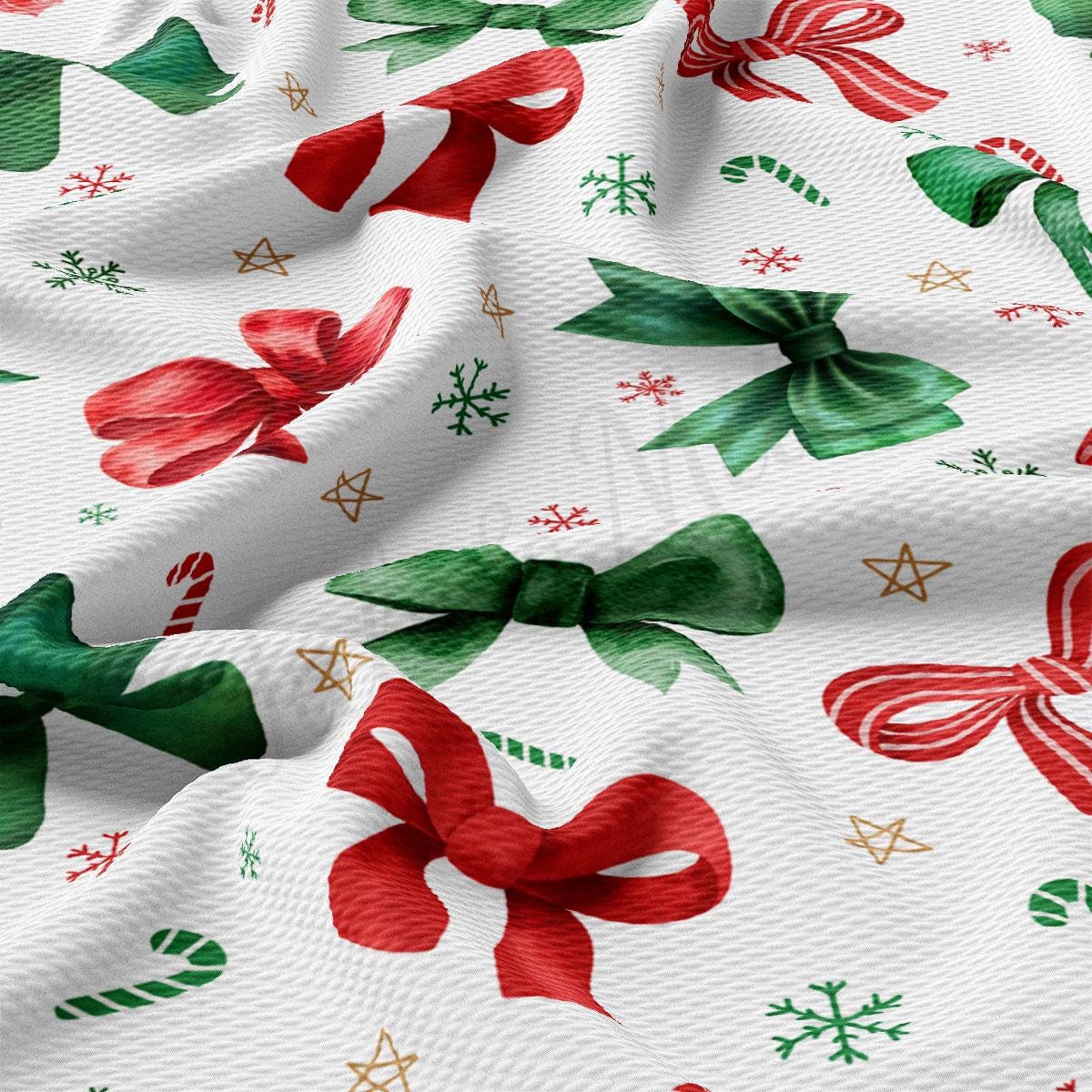 a close-up view of a fabric with a festive Christmas-themed pattern. The pattern includes various Christmas-related elements such as bows, candy canes, snowflakes, and stars, all in a vibrant mix of red, green, and gold colors. The fabric appears to be made of a soft, textured material, giving it a cozy and holiday-inspired appearance.