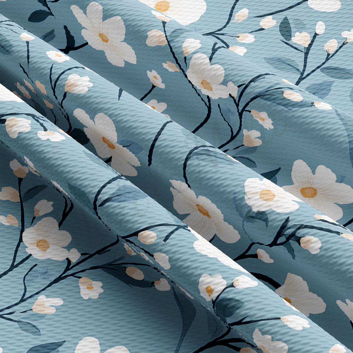 a close-up view of a fabric with a floral pattern of white flowers and green leaves. The fabric appears to be blue, and the pattern is intricate and detailed, with the flowers and leaves filling the entire fabric.