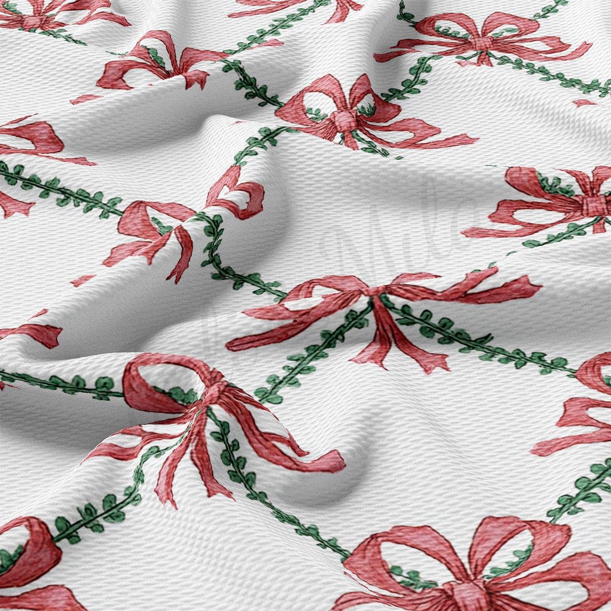 a close-up view of a fabric with a repeating pattern of red bows and green leaves. The bows are arranged in a diagonal pattern, creating a sense of movement and dynamism across the fabric. The green leaves add a touch of nature and freshness to the overall design.