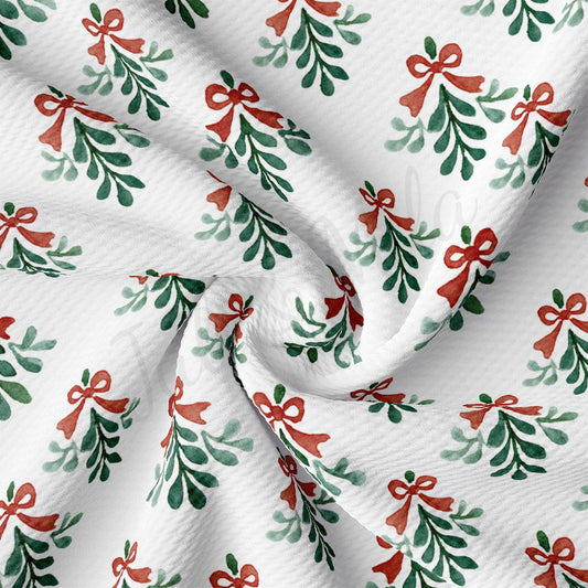 a close-up view of a fabric with a repeating pattern of green and red Christmas-themed designs, including mistletoe and red bows.