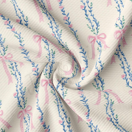 a close-up view of a fabric with a repeating floral pattern of pink bows and blue leaves.