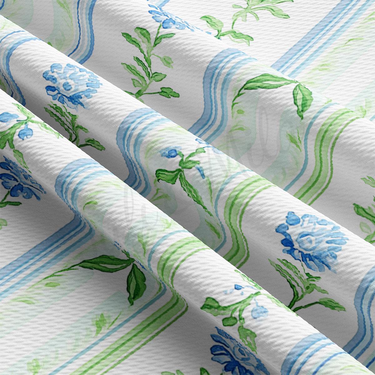 a close-up view of a fabric with a floral pattern in shades of blue and green. The fabric appears to be folded or rolled, revealing the intricate design of the flowers and leaves.