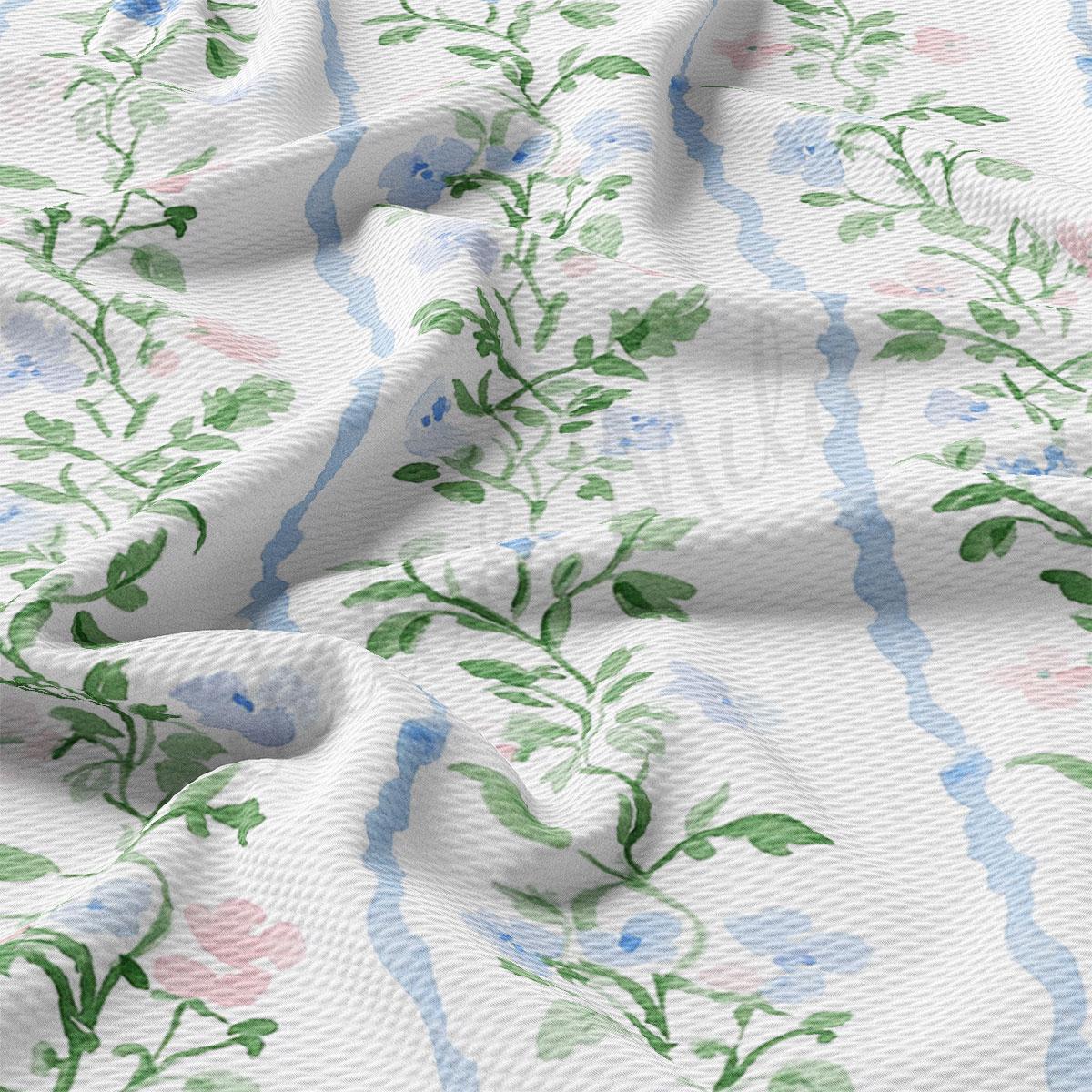 a close-up view of a fabric with a floral pattern, featuring green leaves and flowers in shades of blue and pink. The fabric appears to be crumpled, giving it a soft and delicate appearance.