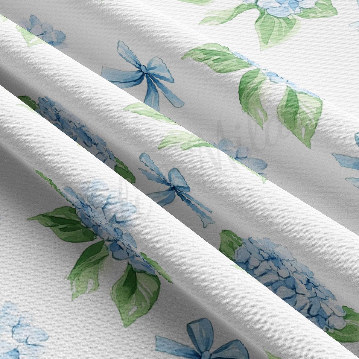 a close-up view of a fabric with a repeating pattern of blue flowers and green leaves. The fabric appears to be white, and the pattern is intricate and detailed, with the flowers and leaves appearing to be hand-painted or printed onto the fabric.