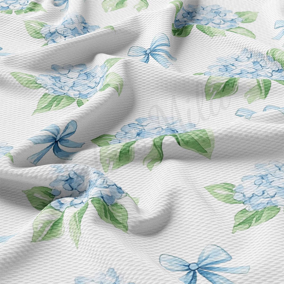 a close-up view of a fabric with a floral pattern of blue hydrangeas and green leaves. The fabric appears to be crumpled, giving it a soft and delicate appearance.