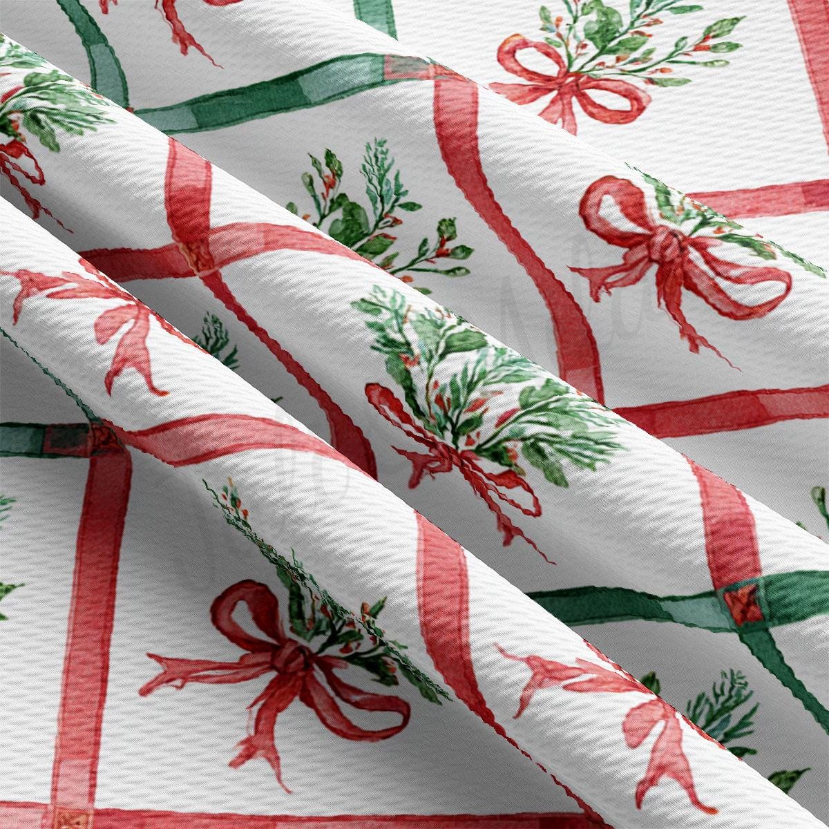 a close-up view of a fabric with a repeating pattern of red and green bows and leaves. The bows appear to be made of ribbon and are arranged in a diagonal pattern across the fabric. The leaves are depicted in a more detailed manner, adding a touch of realism to the overall design. The fabric itself is white, providing a stark contrast to the vibrant colors of the bows and leaves.