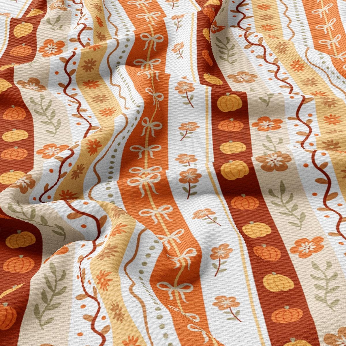a close-up view of a fabric with a repeating pattern of orange and white stripes, along with floral and pumpkin motifs.