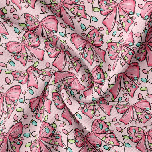 a close-up view of a fabric with a repeating pattern of pink bows and green leaves. The bows are arranged in a diagonal pattern, creating a sense of movement and dynamism across the fabric. The green leaves add a touch of nature and freshness to the overall design. The fabric appears to be made of a soft, plush material, suitable for clothing or home decor.